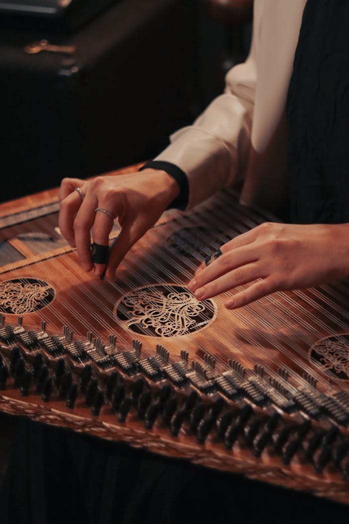 menu-01 An artistic close-up of hands tuning a traditional kanun string instrument, highlighting intricate details.