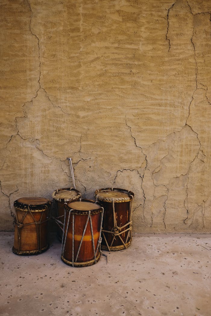 menu-03 Three ethnic drums rest against a textured, rustic wall, capturing cultural essence in Dubai.